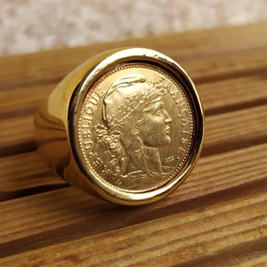 May include: A gold ring with a coin design featuring a woman's profile and the text "REPUBLIQUE FRANCAISE".