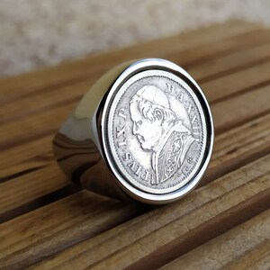 May include: A silver ring with a round coin design featuring a profile of a man with a hat and the text "PIVS IX P. MAXIMIL",