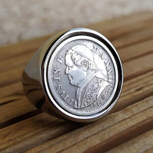 May include: A silver ring with a coin design featuring a portrait of Pope Pius IX. The coin has the inscription "PIVS IX PONT MAX ANNO" around the edge.