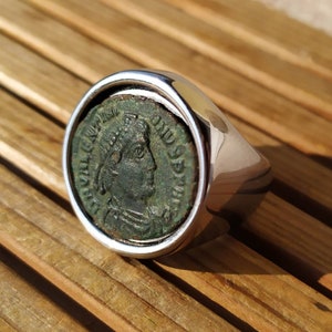 Op de afbeelding: Een zilveren ring met een groene Romeinse munt in het midden. De munt toont het profiel van een persoon met een kroon.