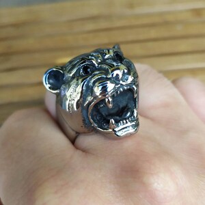 May include: A silver ring featuring a detailed design of a snarling animal head. The animal has black eyes and sharp teeth.
