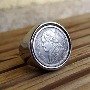 May include: A silver ring with a coin design featuring a profile of Pope Pius IX. The coin is surrounded by a silver band.