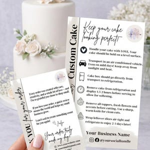 May include: A two-tiered white cake with floral decorations, accompanied by two cards. One card reads "Custom Cake" and provides cake care instructions. The other card says "Thank you for your order" and includes contact information.