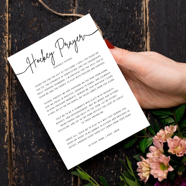 May include: A white card with the words "Hockey Prayer" in elegant script. The card contains a prayer about the game of hockey, with text in black. The card is held by a person's hand, with flowers in the background.