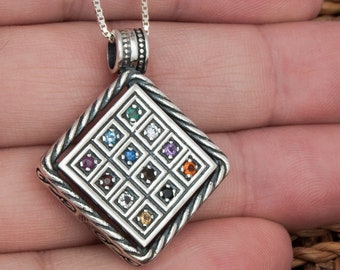 May include: A silver pendant necklace with a square-shaped charm featuring a grid of 16 colorful gemstones. The charm is surrounded by a decorative border.