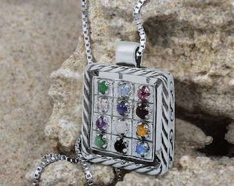 May include: A silver pendant necklace with a square-shaped charm featuring a grid of twelve colorful gemstones. The charm is surrounded by a decorative border.