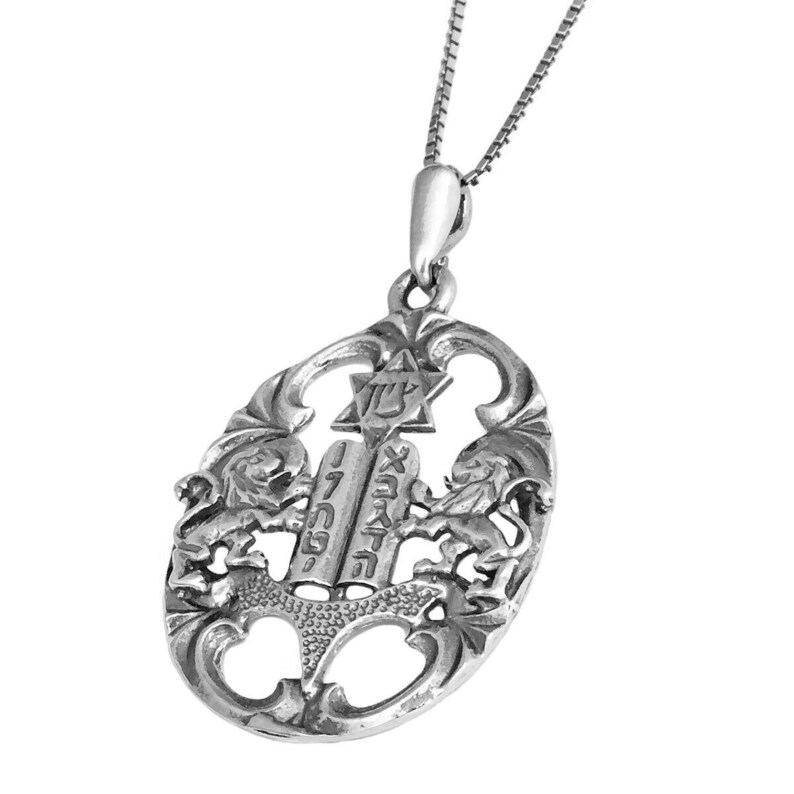 May include: A silver-toned oval pendant on a thin chain. The pendant features an openwork design with two lions flanking a central set of tablets inscribed with Hebrew text. Above the tablets is a Star of David with Hebrew lettering inside.