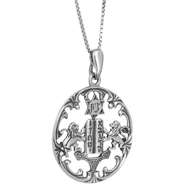 May include: A silver-toned oval pendant necklace featuring an openwork design with two lions flanking a central tablet inscribed with Hebrew text. Above the tablet is a Star of David with a Hebrew character, all suspended from a thin box chain.