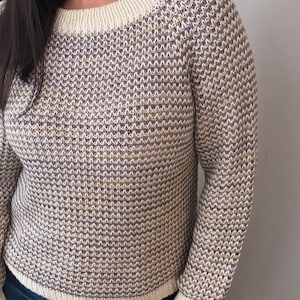 May include: A cream-colored sweater with a subtle brown and gold fleck pattern. The sweater has a round neckline and long sleeves.