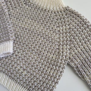 May include: A beige and white knitted sweater with a high neck and long sleeves.