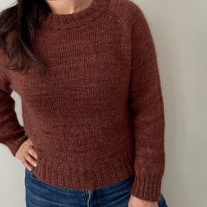 Könnte beinhalten: Ein brauner Strickpullover mit Rundhalsausschnitt und langen Ärmeln.