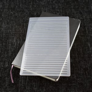 May include: A clear plastic stencil with parallel lines for creating a lined effect on paper or other surfaces.