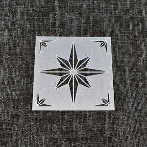 May include: A clear plastic stencil featuring a starburst design. The starburst has 16 points and is centrally positioned within the square stencil.