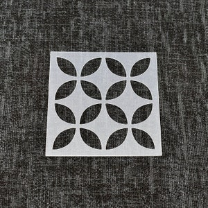 May include: A white plastic stencil featuring a geometric pattern of overlapping circles. The stencil is designed for crafting and decorating projects.