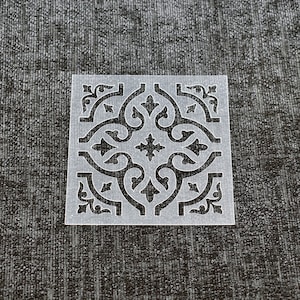 May include: A white plastic stencil featuring an intricate, geometric design. The pattern is reminiscent of a traditional tile design.
