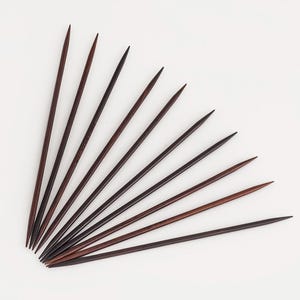 May include: A set of ten long, slender, dark brown wooden knitting needles arranged in a fan shape. Each needle features a smooth, tapered point at one end and a rounded base at the other, showcasing the natural grain and deep color of the wood.