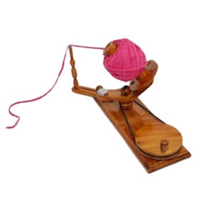 May include: A wooden yarn ball winder with a polished finish, featuring a circular base, a hand-cranked wheel connected by a black belt, and a vertical spindle holding a vibrant pink ball of yarn with a single strand extending outward.