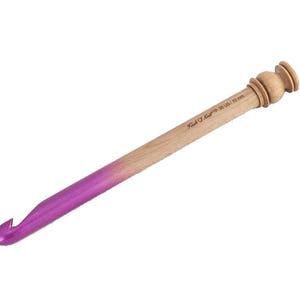 May include: A wooden crochet hook with a smooth, natural light brown finish and a vibrant purple tip. The handle features a decorative knobbed end and is clearly engraved with the text "Furls Crochet" and the size "S US / 19 mm".