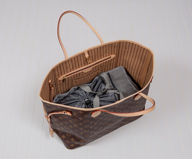 May include: A brown and tan Louis Vuitton tote bag with a gray drawstring bag inside. The bag has a brown leather handle and a gold metal zipper.