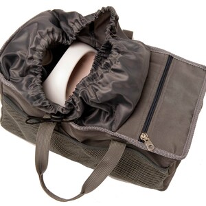 May include: A gray canvas bag with a drawstring top and a zippered pocket. The bag has a mesh panel and two handles. The bag is open and a white object is inside.