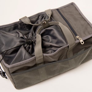 May include: A gray canvas tote bag with a drawstring closure and a mesh pocket on the side. The bag has two top handles and a zippered pocket on the top.
