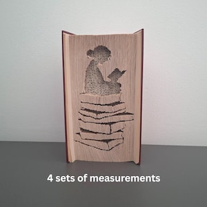 May include: A book sculpture featuring a carved design of a person reading to a child, sitting on a stack of books. The pages are light brown, and the cover is dark red. The text "4 sets of measurements" is at the bottom.