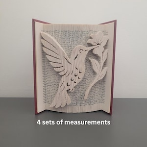 May include: A book sculpture featuring a hummingbird and flower design. The pages are folded to create the image, with a maroon spine. The text "4 sets of measurements" is at the bottom.