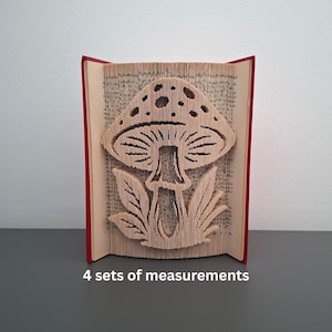 May include: A book sculpture with a mushroom design cut into the pages. The mushroom is beige with dark spots, and the book has red covers. The text "4 sets of measurements" is at the bottom.