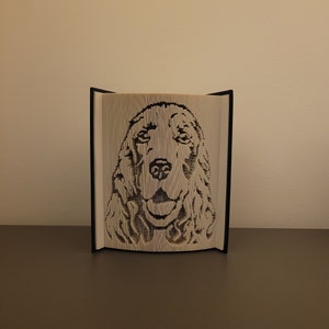 Könnte beinhalten: Eine Buchkunstskulptur eines Hundekopfes, hergestellt durch Falten der Seiten eines Buches. Der Hund hat braunes Fell und schaut direkt auf den Betrachter.