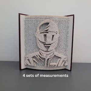 May include: A book sculpture depicting a helmeted figure, crafted by folding the pages of a book. The book has a dark red spine. The text "4 sets of measurements" is visible at the bottom of the image. The artwork is a unique piece.