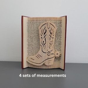 Puede incluir: Escultura de libro con diseño de bota de vaquero. La bota está cortada de las páginas de un libro, con detalles intrincados. El libro tiene una cubierta roja y se muestra sobre una superficie gris. El texto "4 sets of measurements" es visible.