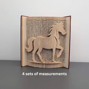 Puede incluir: Escultura de libro con un diseño de caballo tallado en las páginas. El libro abierto muestra la silueta del caballo. El libro tiene una cubierta marrón. El texto "4 sets of measurements" es visible en la parte inferior.