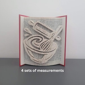 Op de afbeelding: Een uniek boekkunstsculptuur met een bakthema. De pagina's zijn gevouwen om afbeeldingen van een mengkom, garde en deegroller te creëren. Het boek heeft een rode rug en de tekst "4 sets of measurements" onderaan.