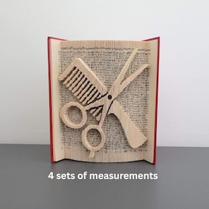 May include: A unique book art sculpture featuring a comb and scissors design, perfect for a hairstylist. The pages are intricately folded to create the comb and scissors. The book has a red spine and is displayed on a gray surface.