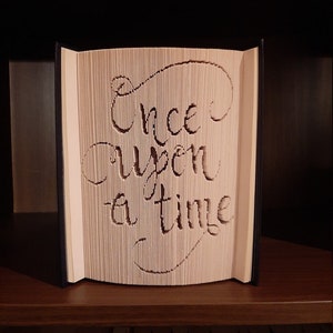 May include: A book with the words "Once upon a time" cut out of the pages. The book is open and standing upright on a shelf.