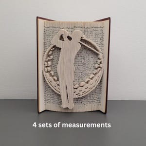 Peut inclure: Sculpture d'art de livre unique représentant une silhouette de golfeur dans un cercle. Les pages sont pliées pour créer l'image, avec une tranche marron foncé. Sur une surface grise.
