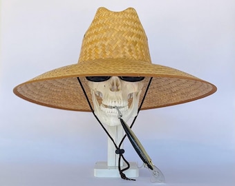 May include: A large, wide-brimmed straw hat with a black chin strap. The hat is worn by a white plastic skull with sunglasses. A fishing lure is hanging from the skull's mouth.