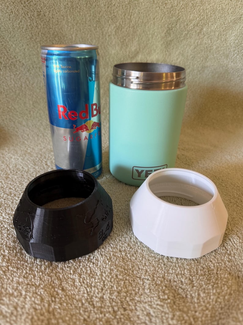 Op de afbeelding: Een assortiment items, waaronder een Red Bull-blikje, een mintgroene ge&iuml;soleerde tumbler en twee beschermende bekerhouders, &eacute;&eacute;n zwart en &eacute;&eacute;n wit. De bekerhouders hebben een geometrisch ontwerp.
