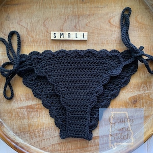 May include: Black crochet bikini bottom with scalloped edges and ties on the sides. The size tag reads "SMALL".