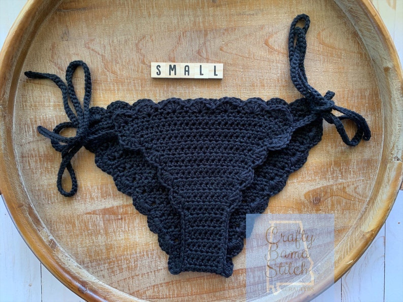 May include: Black crochet bikini bottom with scalloped edges and ties on the sides. The size tag reads "SMALL".