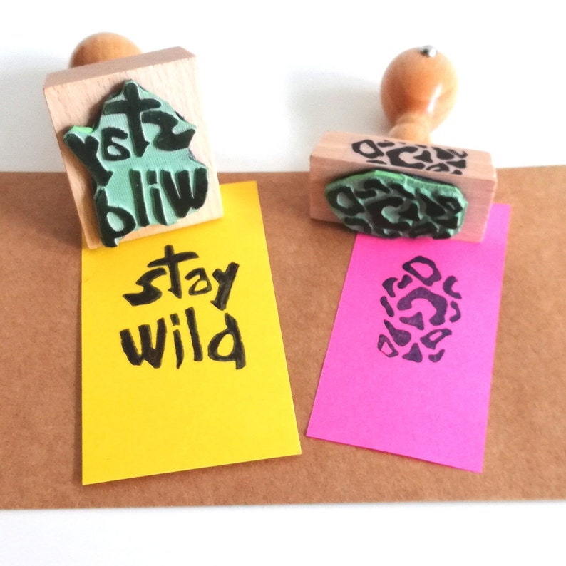 May include: Two wooden stamps with black ink. One stamp has a green and black design with the text "Stay Wild". The other stamp has a green and black leopard print design.