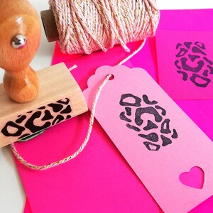 May include: A wooden stamp with a leopard print design, a pink gift tag with a leopard print design, and a spool of pink twine with gold accents.