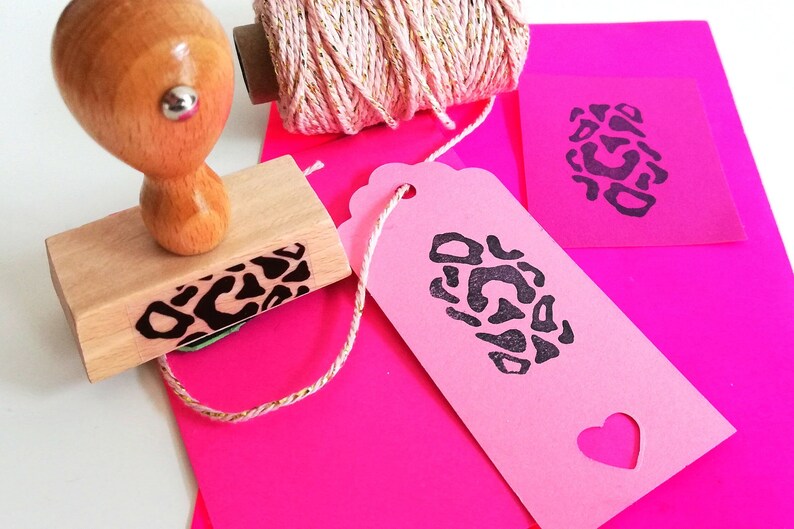May include: A wooden stamp with a leopard print design, a pink gift tag with a leopard print design, and a spool of pink twine with gold accents.