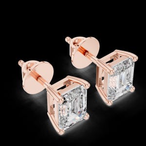 Op de afbeelding: Een paar roségouden oorstekers met vierkant geslepen, heldere edelstenen. De oorbellen hebben een stift- en sluiting. De edelstenen zijn gezet in een vier-klauwzetting. De oorbellen worden getoond tegen een zwarte achtergrond.