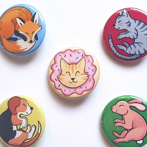 May include: Five colourful round buttons with different animal illustrations. A blue button with a sleeping fox, a red button with a sleeping cat, a yellow button with a cat in a donut, a yellow button with a sleeping dog, and a green button with a sleeping rabbit.