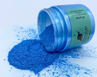 May include: A jar of blue iridescent pigment powder labeled "Astro Dust Premium Mica Powder 20 grams Sky Blue". The jar is tipped over and the powder is spilling out onto a white surface.