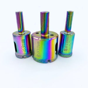 May include: Three iridescent diamond drill bits with silver markings. The drill bits are labeled "Ø 19 mm", "Ø 33 mm", and "Ø 23 mm".
