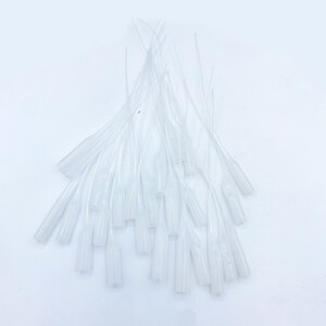 May include: A pile of clear plastic droppers with a pointed tip. The droppers are arranged in a fan shape.