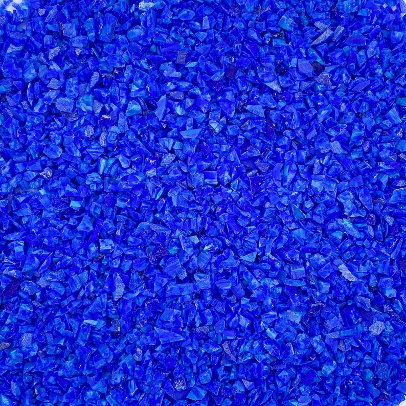 May include: Close-up of a pile of small, irregularly shaped pieces of deep blue glass. The pieces are scattered and reflect light, creating a sparkling effect. The overall texture is rough and fragmented.