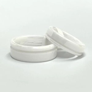 May include: Two white ceramic rings with a grooved design. The rings are stacked on top of each other.